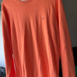 Orange bomullströja Tommy Hilfiger M - Snygg orange långärmad tröja från Tommy Hilfiger i premium bomull. Klassisk rund halsringning och diskret logga på bröstet. Perfekt för dig som vill ha en färgklick i garderoben och gillar stilren design.