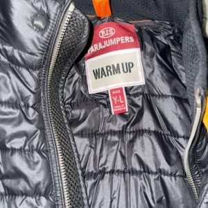 Svart pufferjacka från Parajumpers - Säljer en svart pufferjacka från Parajumpers med quiltad framsida, dragkedja och cool gul detalj vid halsen. Jackan har en bröstficka med dragkedja och broderad logga på ärmen. Perfekt för dig som vill ha en snygg och funktionell jacka.