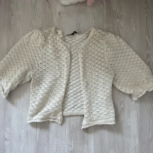 Vit stickad cardigan jacka - Säljer en söt vit stickad cardigan jacka med trekvartsärmar och ett fint hålmönster. Jackan har en luftig och lätt känsla, perfekt för lager på lager. Den är öppen framtill och har en avslappnad passform som ger en chill vibe. 