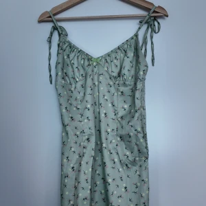 Mintgrön blommig kortklänning med rosett - Supersöt mintgrön kortklänning med små blommor i rosa och gult. Klänningen har smala axelband med knyt, v-ringning och en liten rosett framtill. Materialet är glansigt och känns svalt, perfekt för varma dagar. Smockad rygg för skön passform. Köpte klänningen förra året i Sydkorea som sedan bara legat i garderoben oanvänd. Köpte den för ungefär 600 kr nypris. Pris kan diskuteras  :)