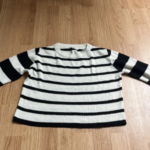 Randig stickad tröja från SAMSA Young - Snygg stickad tröja från SAMSA Young i svart och vitt med klassiskt randigt mönster. Tröjan har rund halsringning och långa ärmar med bredare ränder på ärmarna och smalare ränder på kroppen. Perfekt för dig som gillar en stilren och chill look.