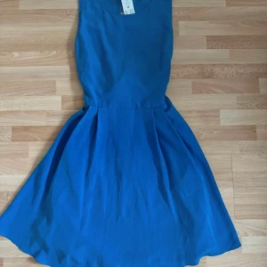 Ny. Blå ärmlös klänning från Gina Tricot - Supersnygg blå klänning från Gina Tricot med markerad midja och stor rosett i ryggen. Klänningen är ärmlös, har rund halsringning och en lätt utställd kjol. Perfekt för dig som vill sticka ut med en färgstark look.