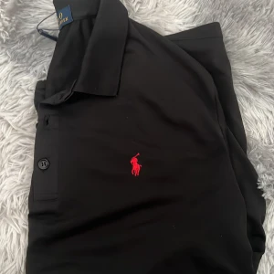Svart pikétröja från Polo Ralph Lauren - Tjenare säljer en svart polo pike är i sportigare material då den är perfekt att golfa eller ha på en varm sommardag den är vuxen Storlek så dem passar runt 165-175cm men den kan nog passa någon som är lite längre hör av er om ni undrar nått!