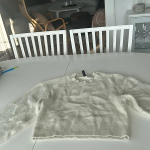 Vit fluffig stickad tröja Divided XS - Supermjuk och fluffig vit stickad tröja från Divided i storlek XS. Tröjan har en croppad passform, rund halsringning och långa ärmar. Perfekt för lager-på-lager och ger en cozy vibe till din outfit.