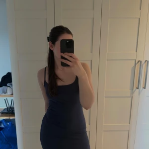 Marinblå långklänning med smala axelband - Säljer en marinblå långklänning med smala axelband och figurnära passform. Klänningen har en enkel och stilren design med rundad urringning och ärmlös modell. Perfekt för dig som gillar minimalistisk och elegant stil.