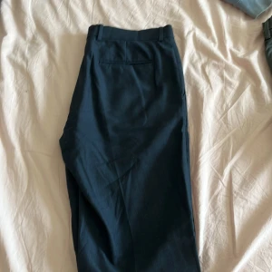 Mörkblå kostymbyxor med knapp - Snygga mörkblå kostymbyxor med klassisk passform och bälteshällor. Byxorna har en enkel bakficka och stängs med knapp och dragkedja framtill. Perfekta för en clean och stilren look.