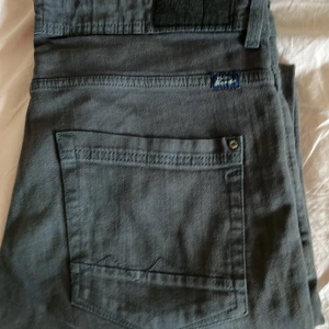 Grå Lee jeans med rak passform - Säljer ett par grå jeans från Lee med klassisk bakficka och diskret logga ovanför fickan. Jeansen har rak passform och är tillverkade i mjukt jeanstyg. Perfekta för en avslappnad och stilren look.