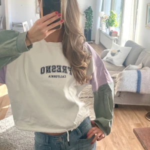 Sweatshirt med färgblock - Säljer en oversized sweatshirt med trycket 'Fresno California' på bröstet. Tröjan är vit med blockfärgade ärmar i ljusgrön och ljuslila, samt dragsko nertill. Perfekt för en chill och trendig look.