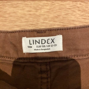 Bruna högmidjade shorts från Lindex - Snygga bruna shorts från Lindex i klassisk femficksmodell med hög midja och bälteshällor. Tillverkade i denim, perfekta för varma dagar. Stängs med knapp och dragkedja framtill och har två bakfickor för en chill look.
