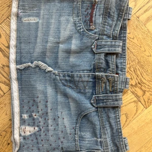 Kort jeanskjol - Säljer en blå jeanskjol från Influence med coola slitningar, broderade detaljer och hjärtan på bakfickorna. Kjolen har bälteshällor, råa kanter och röda dekorationsstygn.  Storlek 10/M men den var väldigt liten i storleken, måtten är : midja rakt över: 39cm och längd : 28 cm 💗