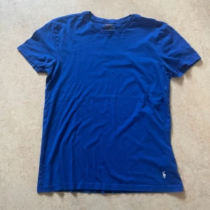 Blå t-shirt från Polo Ralph Lauren - Sällan använd, Klassisk blå t-shirt från Polo Ralph Lauren med korta ärmar och rund hals. Tillverkad i mjuk bomull och prydd med den ikoniska broderade loggan i vitt nertill. Perfekt basic med snygg passform.
