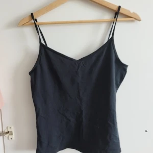 Svart och vit linne topp med smala band - Två stilrena linnetoppar i svart och vitt med smala axelband och v-ringad hals. Perfekta att matcha med jeans eller kjol. Tillverkade i mjuk bomull för en skön känsla hela dagen. M men passar även s