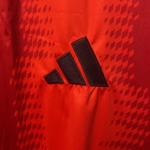 FC Bayern München Adidas matchtröja röd - Röd FC Bayern München fotbollströja från Adidas med svart logga och klubbmärke broderat på bröstet. Tröjan har korta ärmar, V-ringning och ett mönster av röda rutor framtill. Tillverkad i lätt och ventilerande polyester, perfekt för match eller träning, eller mode