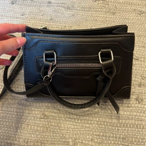 Svart axelväska i skinn med dragkedja - Snygg svart axelväska i skinn med både handtag och avtagbar axelrem. 