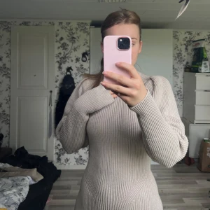 Beige stickad långklänning - Superfin beige stickad långklänning med lång ärm och ribbad struktur. Klänningen har en figurnära passform. Materialet är mjukt och skönt 