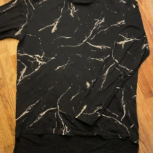 Svart långärmad tröja - Svart långärmad tröja från Jack & Jones Core med unikt marmorliknande mönster i beige. Använd endast ett fåtal gånger. Passar dig som gillar streetwear och vill sticka ut lite extra.🖤🤍