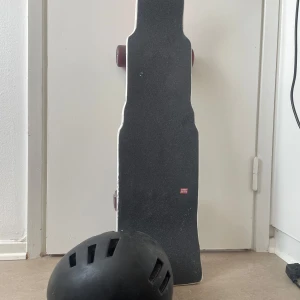 Svart skateboardhjälm med ventiler samt en skateboard  - Säljer denna skateboard plus en svart hjälm med flera ventiler för bra luftflöde, perfekt för skate eller cykel. Hjälmen har en rundad form och är tillverkad i tålig syntet. Snygg och enkel design som passar till streetstyle och action. Pang pris ! 