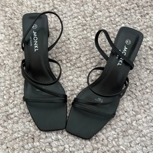 Svarta sandaler med smala remmar från Monki - Stilrena svarta sandaler från Monki med smala remmar och fyrkantig tå. Veganskt material och minimalistisk design som ger en modern vibe. Perfekta för dig som gillar enkel men trendig stil. Aldrig använda!