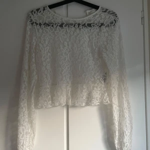 Vit spetsblus från H&M - Superfin vit blus från H&M i genombruten spets med blommigt mönster. Långärmad modell med lätt volang nertill och rund halsringning fram, samt v-ringning bak. Säg till om ni vill se hur den sitter på bara💕
