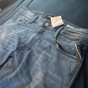 Replay Anbass blå jeans, stl 32 - Snygga blå Replay Anbass jeans i klassisk femficksmodell. Jeansen har en normal passform och är tillverkade i mjukt denimtyg med Replay-logga vid fickan. Perfekta för dig som gillar stilrena och bekväma jeans med modern känsla.