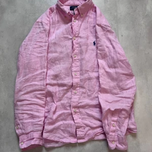 Rosa linneskjorta från Polo Ralph Lauren - Ser bättre ut i verkligheten! Använd få gånger – mycket bra skick. Ej struken på bild.  Rosa skjorta från Polo Ralph Lauren ✅ 100% linne ✅ Storlek: XS–S herr / Barn 14–16 ✅ Skick: 9/10 ✅ Köpt för 1000kr+  Luftig och stilren skjorta med button-down-krage, lång ärm och broderad logga på bröstet. Perfekt för en fräsch och avslappnad look!  📩 Skriv i DM vid frågor eller prisförslag! 