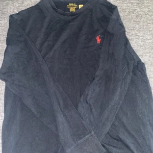 Svart långärmad tröja Polo Ralph Lauren - Svart långärmad tröja från Polo Ralph Lauren med klassisk passform. Tröjan har rund halsringning och den ikoniska röda broderade loggan på bröstet. Perfekt basic att ha i garderoben.