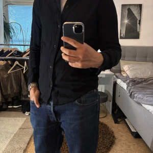 Svart skjorta från Weekday i bomull - Stilren svart skjorta från Weekday i mjuk bomull. Klassisk krage, knäppning framtill och långa ärmar. Perfekt till jeans eller chinos för en clean look. Skjortan har en normal passform och är enkel att matcha med det mesta.