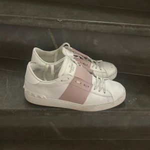 Valentino skor rosa   - Snygga Valentino Garavani Open sneakers i vitt skinn med bred rosa läderdetalj över mitten. Jätte bra skick, box, dustbag medföljer. Kvitto kan kanske letas fram. 
