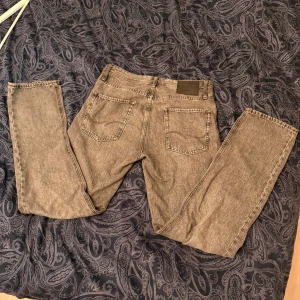 Grå jeans från Jack & Jones Relaxed/Chris - Säljer ett par grå tvättade jeans från Jack & Jones, modell Relaxed/Chris. Jeansen har fem fickor, raka ben och klassisk knappgylf. De är tillverkade i bomull och har en avslappnad passform med normal midja. Perfekta för en chill och stilren look.
