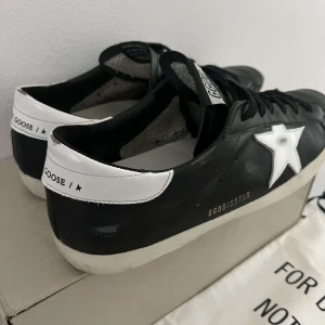 Golden Goose svarta  - Golden Goose sneakers i svart skinn med vit stjärndetalj på sidan och vit hälkappa. Klassisk låg modell med svarta snören och slitna detaljer för en cool, urban look. Perfekta för dig som gillar streetstyle och vill sticka ut. Nypris 5599 kr köpta från NK för cirka 2 månader sedan så knappt använda. Hör av er för fler frågor. Dustbags och påse och allt ingår.