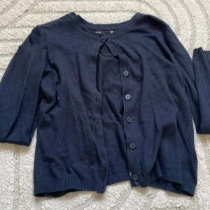 Mörkblå kofta från lager 157, storlek M - Mörkblå kofta från lager 157 i storlek M. Klassisk rund halsringning, knäppning framtill med matchande knappar och ribbade muddar. Perfekt att slänga över en t-shirt eller linne för en chill look.