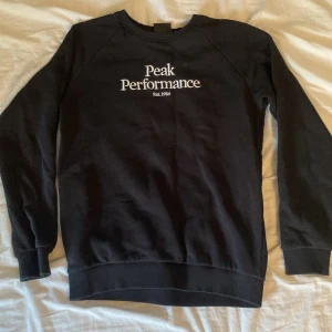 Svart Peak Performance sweatshirt - Svart sweatshirt från Peak Performance med vit broderad logga på bröstet. Klassisk rund halsringning och ribbade muddar vid ärmslut och nederkant. Perfekt för en chill och sportig stil.