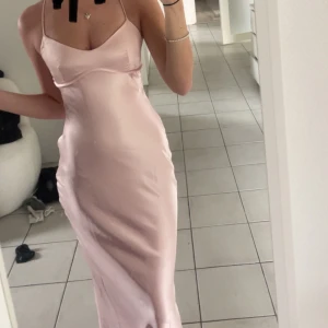 Ljusrosa långklänning i satin -  ljusrosa långklänning med tunna axelband och figurnära passform. 