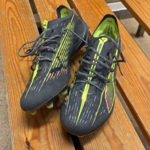 Puma Ultra fotbollsskor svart/gul - Säljer ett par grymma Puma Ultra elite fotbollsskor i svart med neon-gula detaljer och tunna vita linjer. Skorna har snörning, låg profil och mönstrad ovandel i syntetmaterial för bästa grepp och känsla på planen. Perfekta för dig som vill sticka ut på matchen. Pris kan såklart diskuteras. 