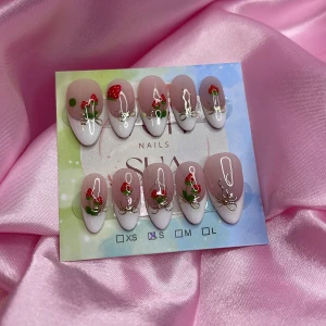 Strawbabe(S);Medium Almond - Superfina gelé press on-naglar i en medium mandelform med fransk tipp och handmålad röd svampdesign samt silvriga detaljer. Basen är nude/rosa och tipparna är vita. Kommer i storlek S: 15 mm, 11,5 mm, 12 mm, 11 mm, 9 mm , perfekta för att snabbt fixa snygga naglar hemma.