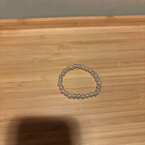 Pärlarmband med vita pärlor - Stilrent armband med vita pärlor på elastisk tråd. Perfekt accessoar för att ge din outfit en klassisk och elegant touch. Passar både till jeans och klänning och är lätt att matcha med andra smycken.