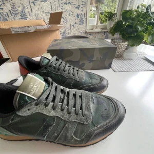 Valentino Garavani Rockrunner sneakers - Snygga Valentino Garavani Rockrunner sneakers i grönt camouflagemönster med detaljer i mocka, skinn och textil. Skorna har svarta snören, röd häl och turkos detalj vid sulan. Perfekt för dig som vill sticka ut med exklusiva och trendiga sneakers. PRIS KAN DISKURERAS