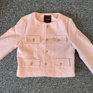 Ljusrosa kavajjacka från Alessa, Naked Blazer - Snygg ljusrosa kavajjacka från Alessa med guldknappar och fyra fickor framtill. Jackan har en rak, croppad passform och är tillverkad i ett strukturerat tyg som ger en exklusiv känsla. Perfekt för dig som vill sticka ut med en chic och trendig look.