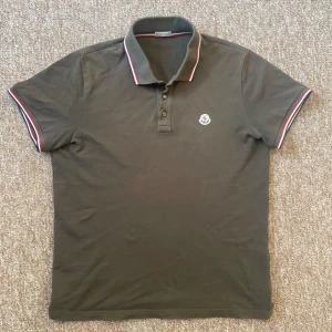 Olivgrön Moncler piké - Säljer en olivgrön pikétröja från Moncler med klassisk krage och knäppning framtill, kan garantera äkthet till 100% då jag köpte den i butik, köpt förra våren och använt sparsamt, otroligt fint skick 9,5/10 inga defekter, inga fläckar och inga tecken på slitage alls. Priset är såklart diskuterbart som alltid mina vänner ❤️🫶