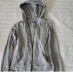 Grå hoodie med dragkedja - En klassisk grå hoodie från Jack & Jones med dragkedja framtill och två stora fickor. Tröjan har huva med dragsko och långa ärmar. Perfekt för chill dagar eller när du vill ha en enkel och stilren look. Priset är diskuterbart och tveka inte att höra av dig privat om frågor eller funderingar! Sömmen har gått upp på vänstra fickan men går nog att lösa snabbt för den som kan sy. 