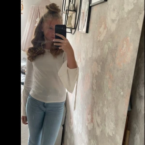 Vit ribbad topp med trumpetärm Gina Tricot - Supersnygg vit ribbad topp från Gina Tricot med långa trumpetärmar och knytband vid ärmsluten. Figurnära passform och rund halsringning. Perfekt att styla med jeans eller kjol för en trendig look.