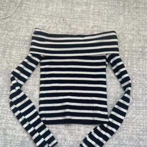 Randig offshoulder topp i ribbad bomull - HELT NY TOG ALDRIG PÅ MIG DEN Snygg svartvit randig offshoulder topp med långa ärmar. Ribbad struktur som ger en cool och trendig look. Perfekt att styla med jeans eller kjol för en chill vibe.