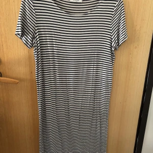 Randig t-shirtklänning från Pieces - Snygg t-shirtklänning från Pieces i svart och vitt med klassiskt horisontellt randigt mönster. Modellen är rak och har korta ärmar samt rund halsringning. Perfekt för en chill och stilren look.