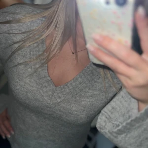 Grå stickad tröja med v-ringning - Säljer en mysig grå stickad tröja med v-ringning och långa ärmar. Perfekt för kyligare dagar. Tröjan har en bekväm passform och ribbade muddar vid ärmslut och nederkant💗