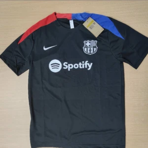 FC Barcelona svart Nike fotbollströja priset kan diskuteras  - Snygg svart FC Barcelona fotbollströja från Nike med korta ärmar. Tröjan har klubbmärke och Spotify-logga på bröstet samt röda och blå detaljer på axlarna. Tillverkad i lätt och ventilerande material, perfekt för match eller träning.