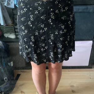 Svart blommig kjol från XOXO Friends - Supersöt svart kortkjol från XOXO Friends(Ullared) med små blommor i lila och gult. Kjolen har en lätt plisserad look och resår i midjan för skön passform. Perfekt för dig som gillar en feminin och chill stil.