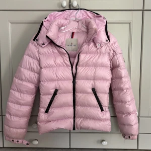 Ljusrosa Moncler jacka - Superfin ljusrosa dunjacka från Moncler med svart dragkedja och fickor.  Säljer då den blivit lite liten för mig:( Små fläckar som man ser på bilden, men inget märkbart. 😆❤️ Det är storlek 12 i barnstorlek men tycker den passar en XS/S. 