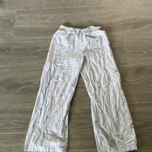 Randiga vita linnebyxor från H&M - Lätta och luftiga vita linnebyxor från H&M med diskreta ljusblå ränder. Byxorna har elastisk midja med snörning för extra komfort och är tillverkade i mjuk bomull. Perfekta för chill dagar eller när du vill ha en avslappnad look.