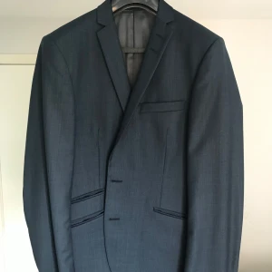 Mörkblå kostymset från Tiger of Sweden - Snygg mörkblå kostym set från Tiger of Sweden med klassisk passform. Kavajen har tre framfickor, innerfickor och stilren design. Fodret är grått och materialet känns exklusivt, perfekt för dig som vill ha en tidlös look. Byxstorlek 52