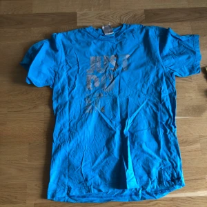 Blå Nike t-shirt med tryck - Snygg blå t-shirt från Nike med det klassiska 'Just Do It'-trycket framtill. T-shirten har rund hals och korta ärmar, perfekt för en sportig look. Tillverkad i mjuk bomull som känns skön mot huden.